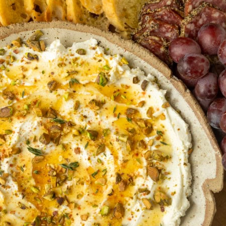 whipped goat cheese appetizer in a pottery bowl with crostini, salami, and grapes