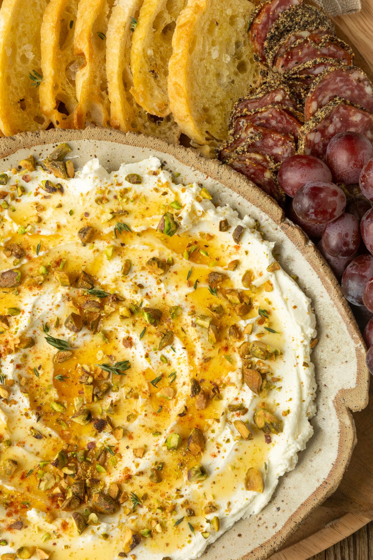whipped goat cheese appetizer in a pottery bowl with crostini, salami, and grapes