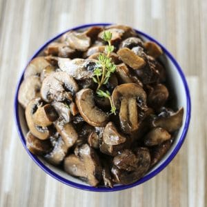 blue edged, white ceramic bowl, wooden tile background, simple garlic butter sauteed mushrooms, sprig of fresh thyme