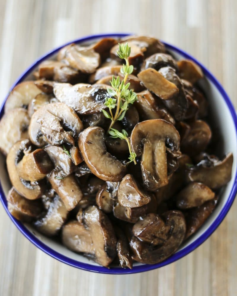 blue edged, white ceramic bowl, wooden tile background, simple garlic butter sauteed mushrooms, sprig of fresh thyme