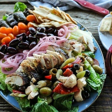 Greek Salad with lemon garlic chicken, marinated olive salad, quick pickled red onions, crumbled feta cheese, garlic stuffed kalamata olives, tiny grape tomatoes, stuffed grape leaves, Greek salad dressing, pita chips as croutons, and a hearty dollop of hummus. This salad will fill you up with sunshiny goodness without making you feel like a slug. The post includes instructions on how to pack these salads up to four days ahead of time for work-week and school lunches.