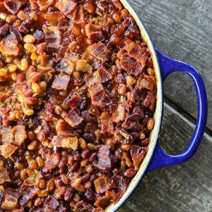 Le Creuset cobalt blue braiser, baked beans, crispy bacon, barbecue sauce, wooden bench