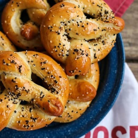 Sourdough soft pretzels in traditional shape, brushed with butter, black and white sesame seeds and kosher salt, on blue and white enamel plate red and white cotton towel, wooden bench