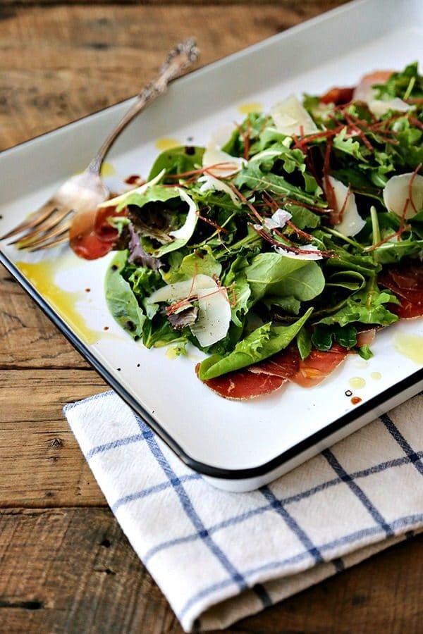 Bresaola Parmesan Salad on white quarter sheet pan with cobalt blue rim, blue and white tea towel, antique fork, rustic wood tabletop