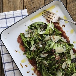 Bresaola Parmesan Salad on white quarter sheet pan with cobalt blue rim, blue and white tea towel, antique fork, rustic wood tabletop