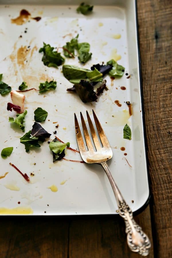 antique fork, mostly empty serving Bresaola Parmesan Salad on white quarter sheet pan with cobalt blue rim, blue and white tea towel, rustic wood tabletop