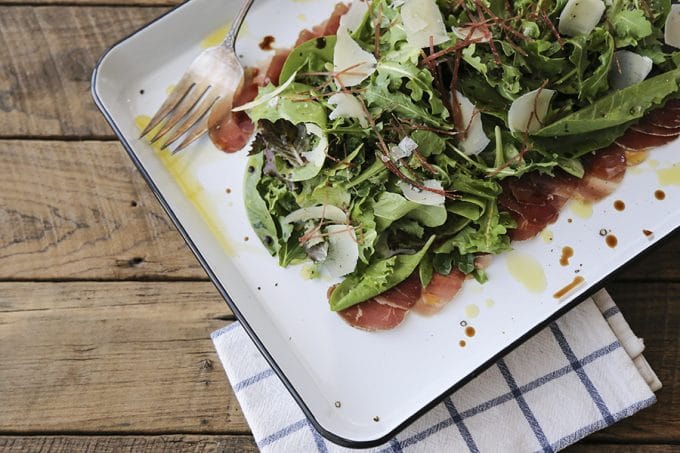 Bresaola Parmesan Salad on white quarter sheet pan with cobalt blue rim, blue and white tea towel, antique fork, rustic wood tabletop