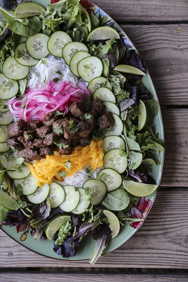 Bo Luc Lac -Shaking Beef- is a spectacularly fresh and flavourful Viêtnamese salad of mixed greens, cucumbers, pickled red onions, juicy mango, tender rice vermicelli noodles, bright herbs, and an irresistible black pepper lime dressing.