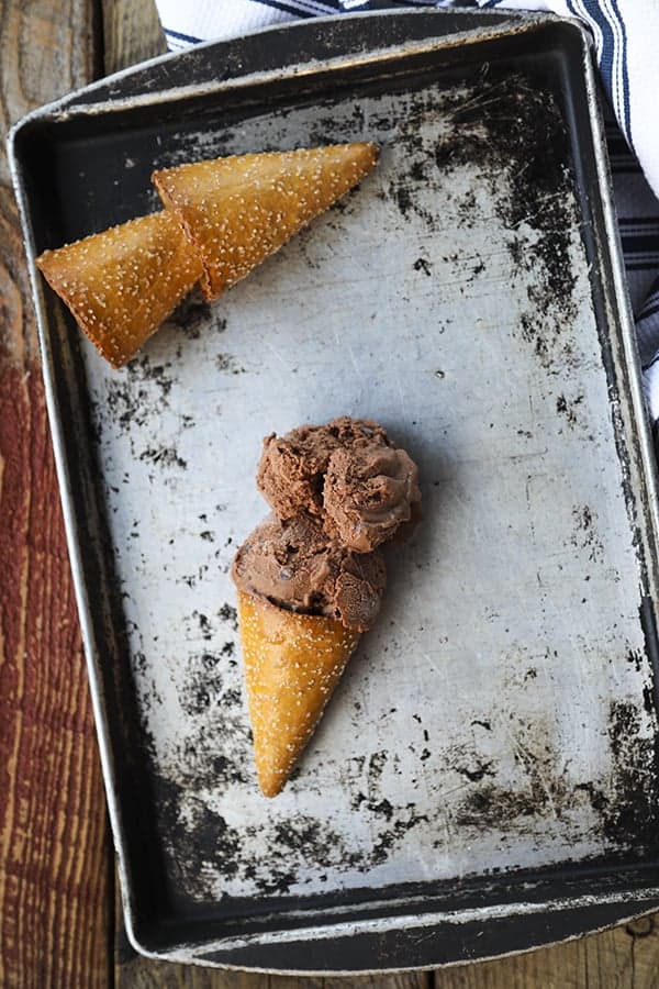 Two scoops of vegan dairy free chocolate ice cream in a pretzel cone on an antique sheet pan.