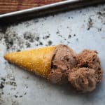 Two scoops of vegan dairy free chocolate ice cream in a pretzel cone on an antique sheet pan.