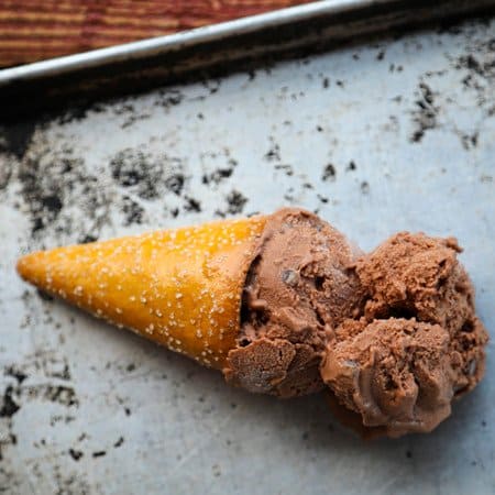 Two scoops of vegan dairy free chocolate ice cream in a pretzel cone on an antique sheet pan.