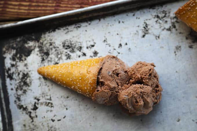 Two scoops of vegan dairy free chocolate ice cream in a pretzel cone on an antique sheet pan.