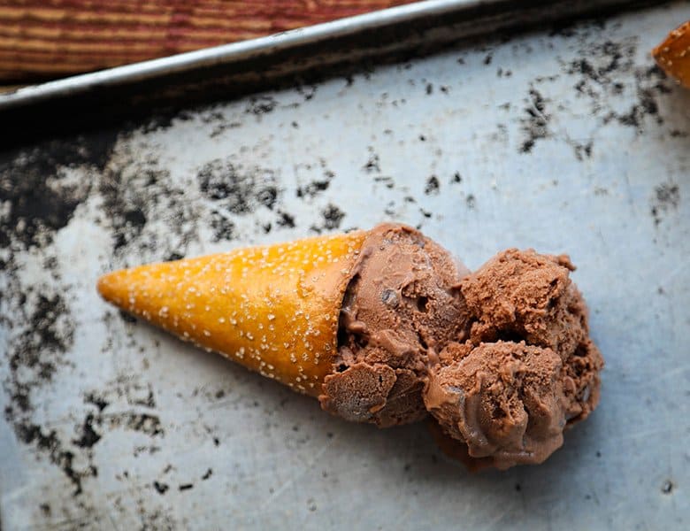 Two scoops of vegan dairy free chocolate ice cream in a pretzel cone on an antique sheet pan.