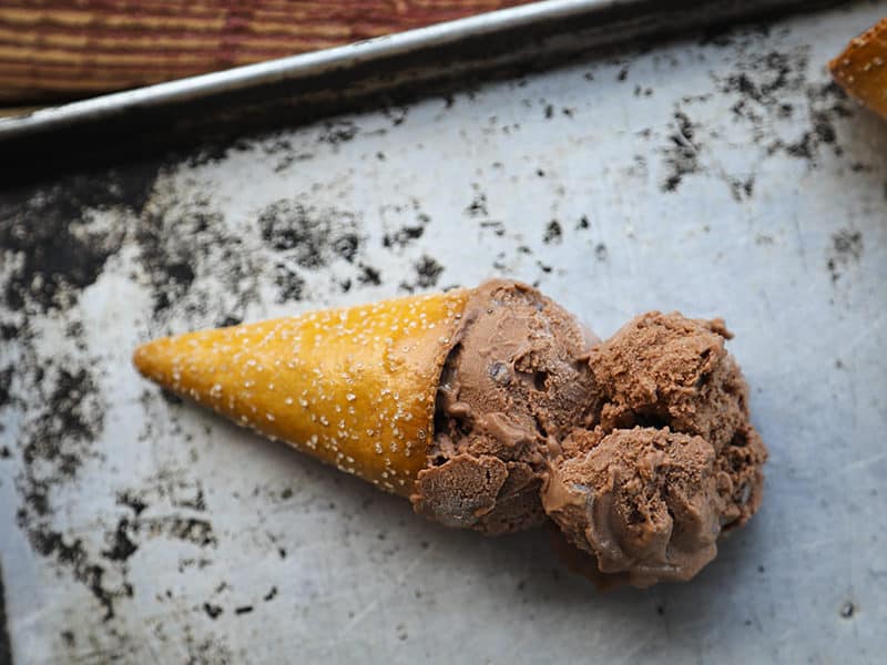 Two scoops of vegan dairy free chocolate ice cream in a pretzel cone on an antique sheet pan.