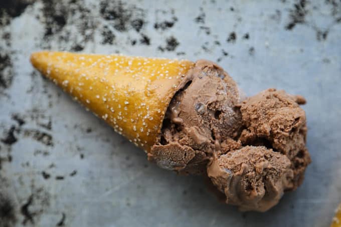 Two scoops of vegan dairy free chocolate ice cream in a pretzel cone on an antique sheet pan.