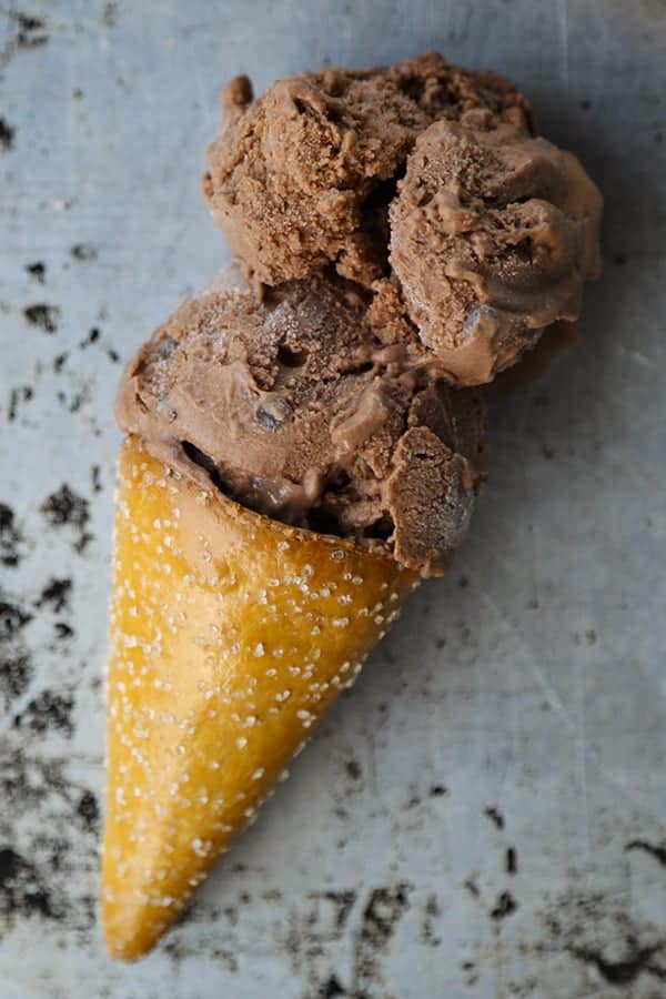 Two scoops of vegan dairy free chocolate ice cream in a pretzel cone on an antique sheet pan.