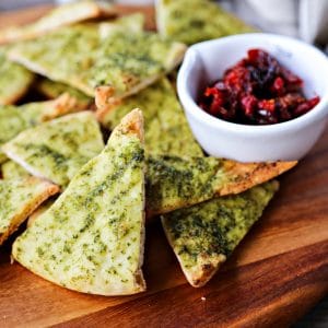 This crispy, crunchy, perfect pesto brushed homemade pita chips recipe is as easy as cut, brush, bake and makes a great snack or salad accompaniment.