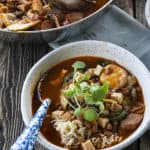 Korean Army Stew or Budae Jjigae in a white bowl with an egg yolk and a blue enamel spoon.