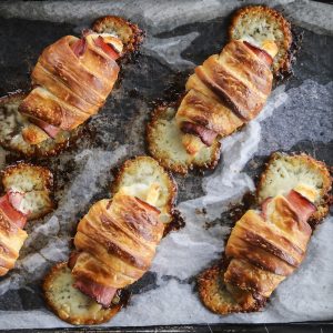 Ham and Cheese Croissants baked on parchment and metal sheet pan, crisp melted cheese running from ends, toasted ham, dark edges ham, pools melted cheese