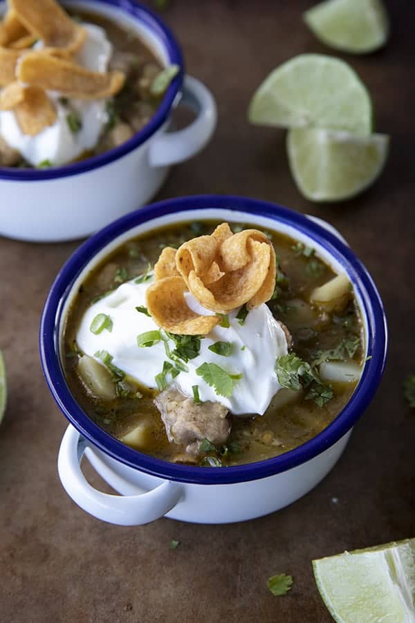 PORK GREEN CHILI IN A WHITE ENAMEL BOWL WITH A BLUE RIM AND HANDLES