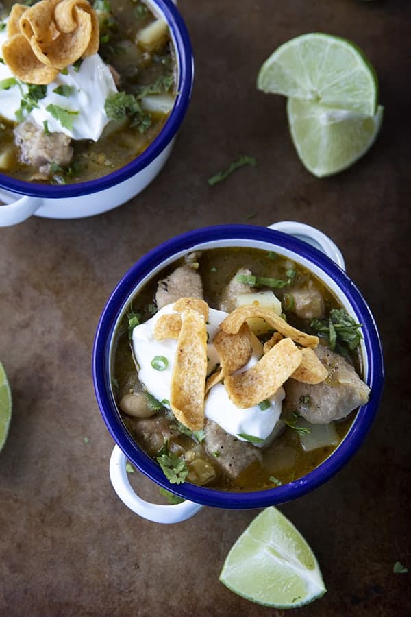 PORK GREEN CHILI IN A WHITE ENAMEL BOWL WITH A BLUE RIM AND HANDLES