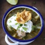 PORK GREEN CHILI IN A WHITE ENAMEL BOWL WITH A BLUE RIM AND HANDLES