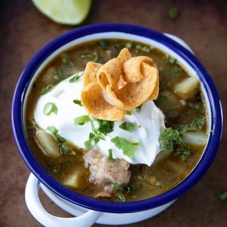 PORK GREEN CHILI IN A WHITE ENAMEL BOWL WITH A BLUE RIM AND HANDLES