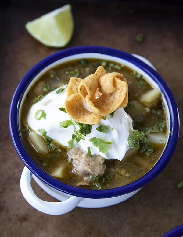 PORK GREEN CHILI IN A WHITE ENAMEL BOWL WITH A BLUE RIM AND HANDLES