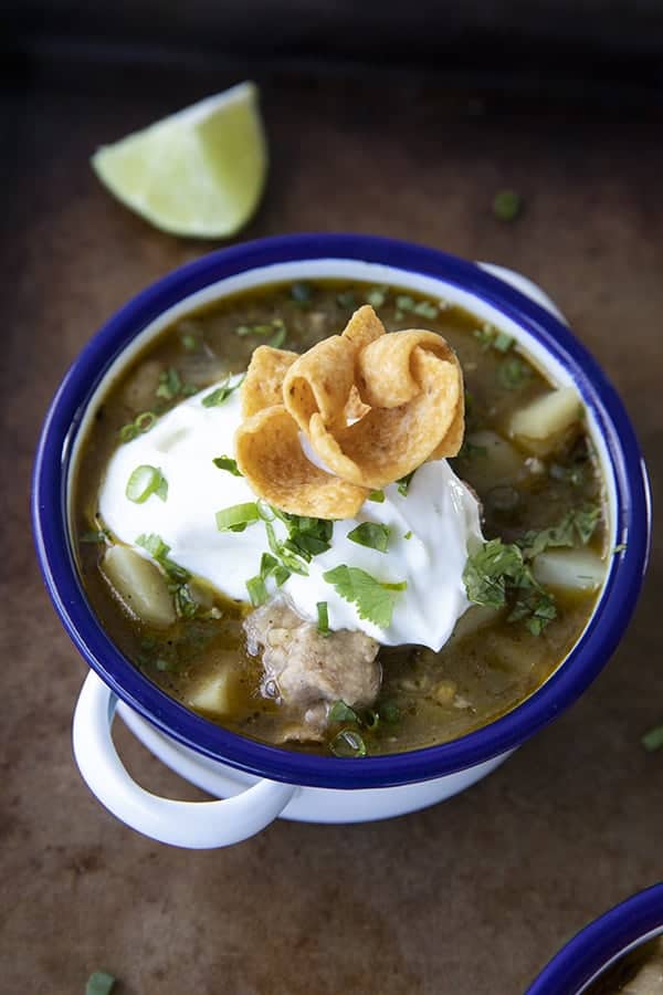 PORK GREEN CHILI IN A WHITE ENAMEL BOWL WITH A BLUE RIM AND HANDLES