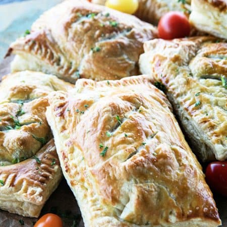 Breakfast Hot Pockets: puff pastry filled with cheesy scrambled eggs and sausage links on a cutting board with cherry tomatoes.