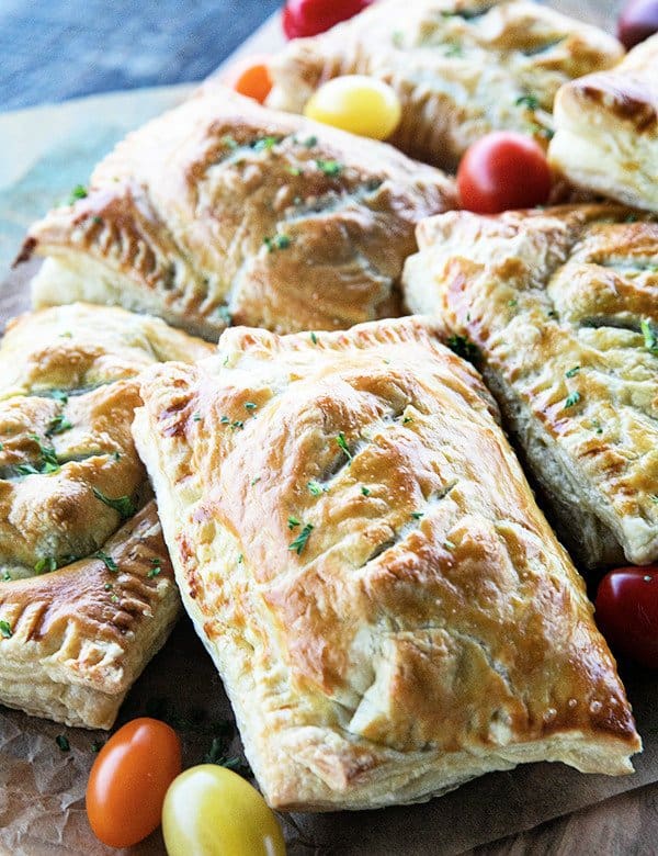 Breakfast Hot Pockets: puff pastry filled with cheesy scrambled eggs and sausage links on a cutting board with cherry tomatoes.